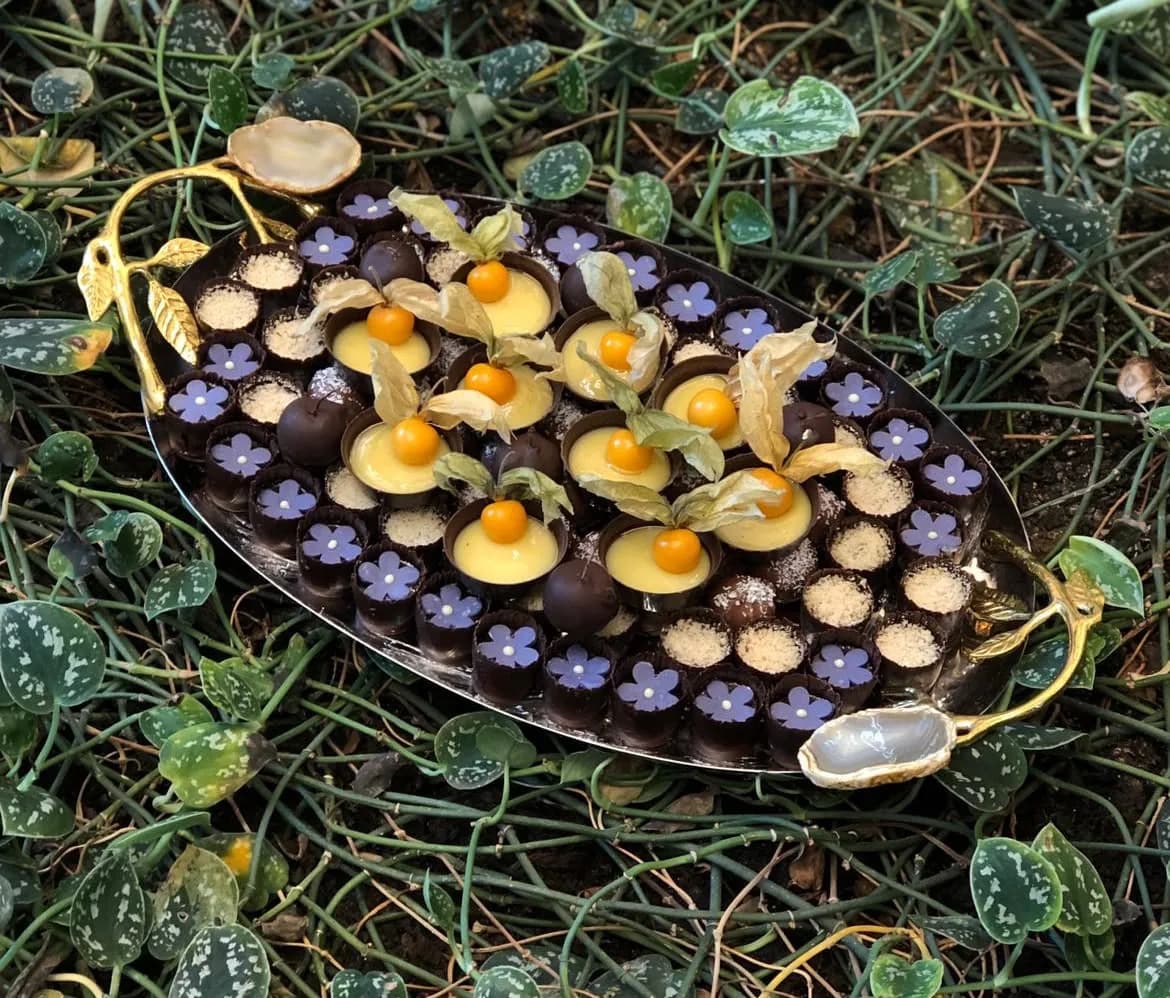 Oval gümüş tepside mor çiçek işlemeli çikolatalar ve physalis